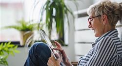 Senior woman sitting on floor at home using digital tablet.