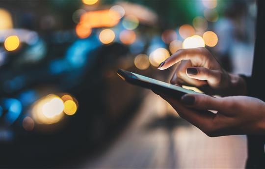 Businesswoman with smartphone using application for calling taxi online walking on city street night