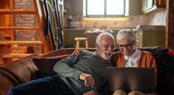 an older gentleman and woman laugh while looking at a laptop screen