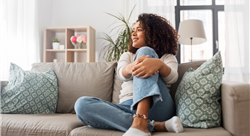 woman sitting on couch in a room full of natural light and appearing happy