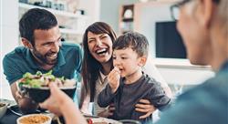 Dad, mom and son having a meal and smiling as they are passing the food to grandma