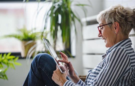 Senior woman sitting on floor at home using digital tablet.