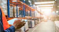 person in orange safety vest holding tablet and checking the stock products in a warehouse