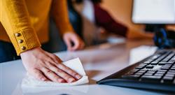 Woman in yellow sweater using a disinfectant wipe to clean desk area