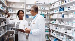 one female pharmacist and one male pharmacist in white coats talking to each other in pharmacy stock room