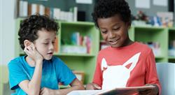 two boys smiling, reading and studying together in their classroom